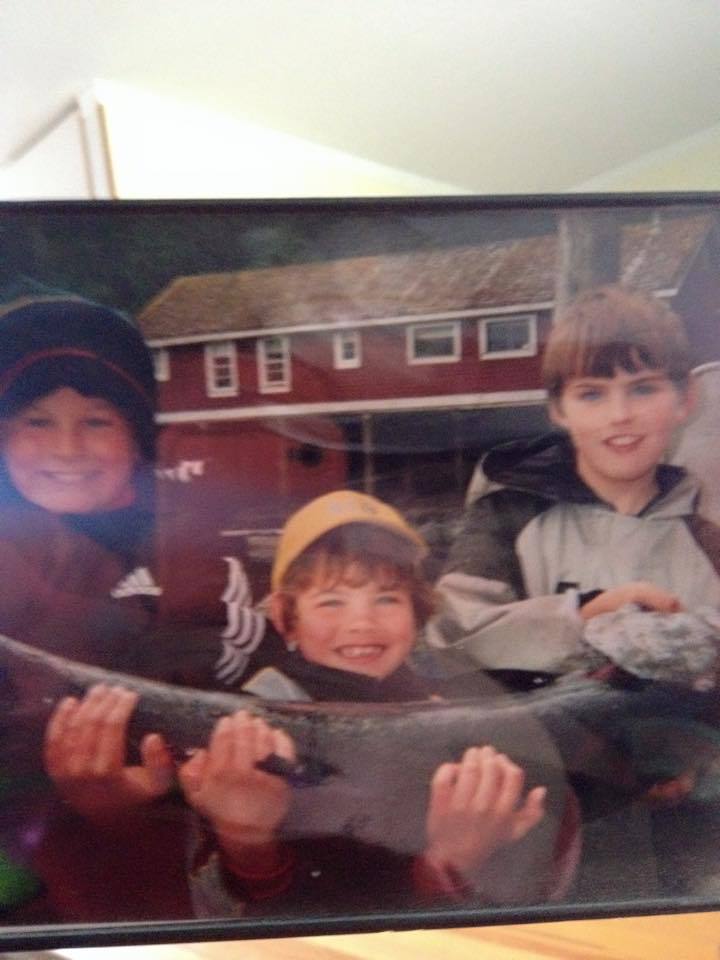 Three children smiling and holding a large fish outdoors in front of a house
