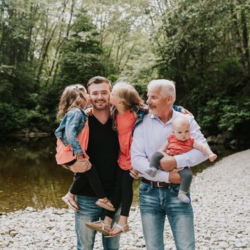 Family of four posing by a river in a wooded area, with two children being held by adults.