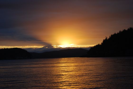 Golden sunset over a calm lake, with dark silhouetted hills and glowing reflections on the water