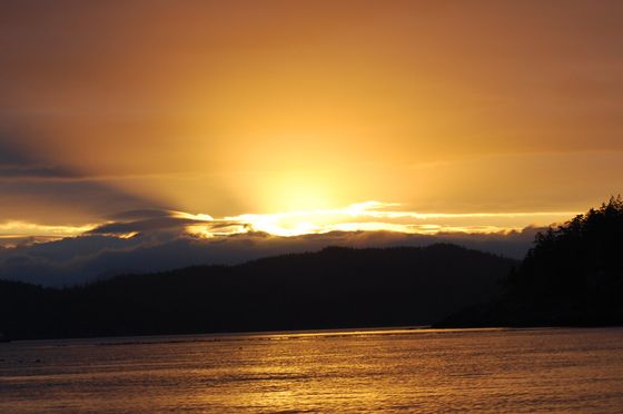 Golden sunset over dark mountains and a calm lake, with glowing clouds and reflections on the water