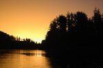 Sunset over a calm river, with dark silhouetted trees along the shore