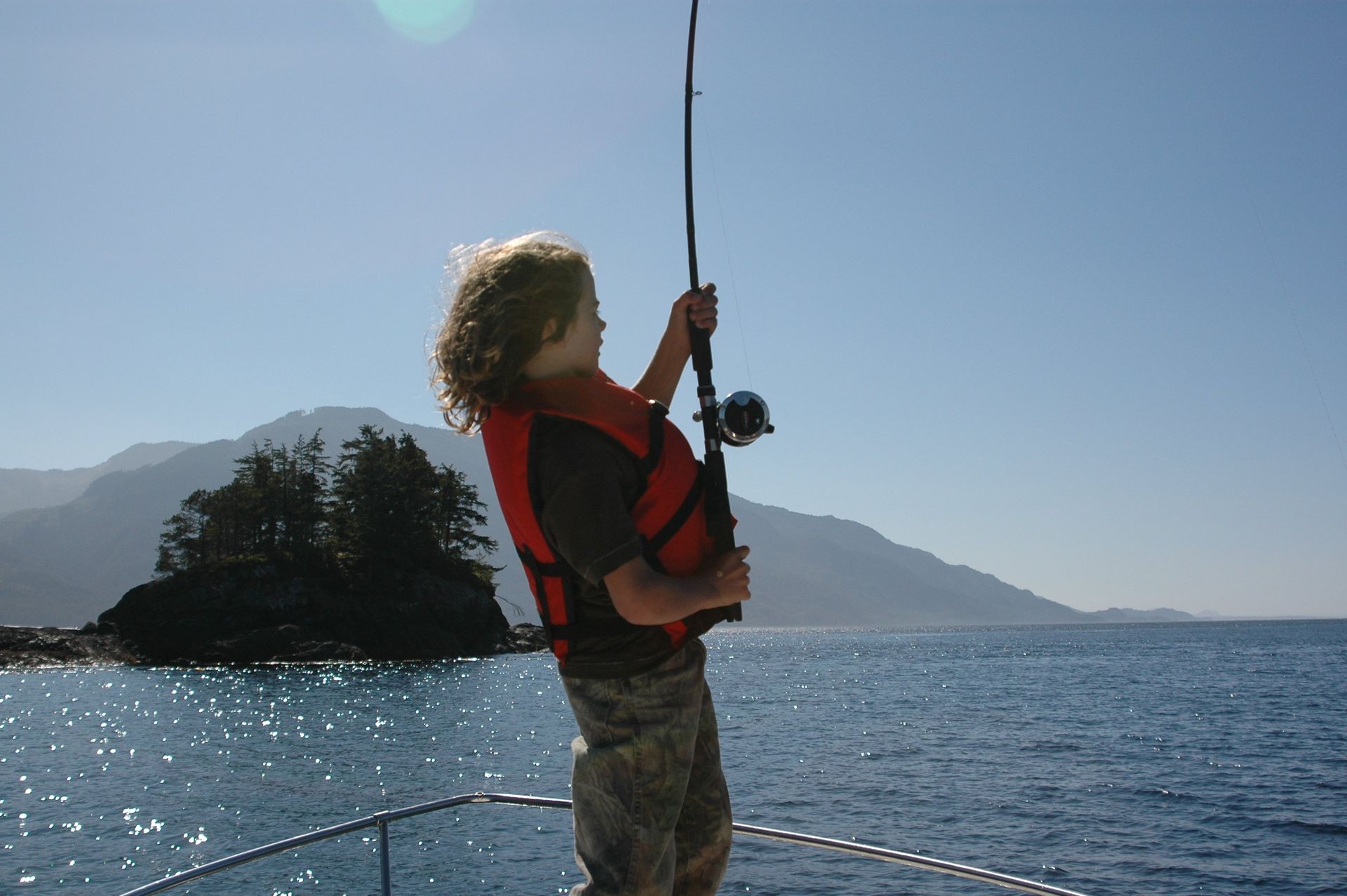 Person sailing, holding a rope on a boat with ocean and mountains in the background