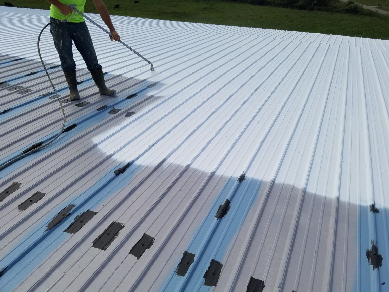 a man spraying white paint on a metal roof