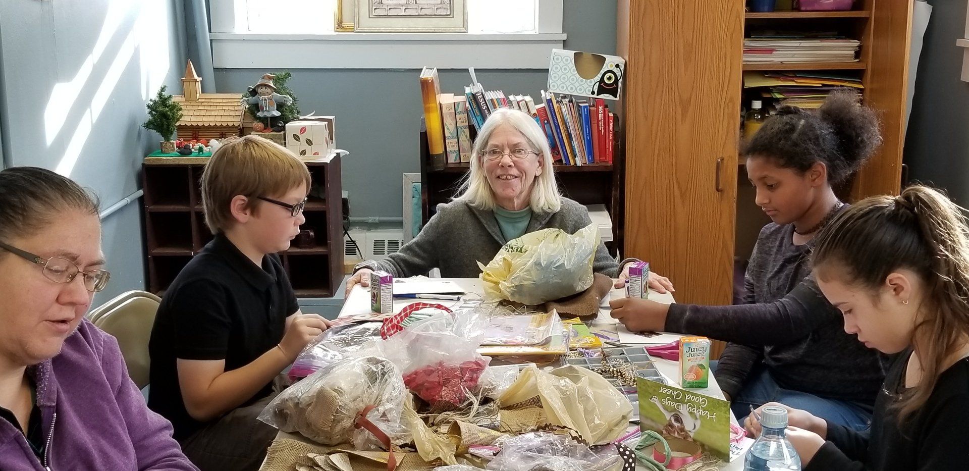 People crafting at a table with a woman smiling at the center. Interior setting.