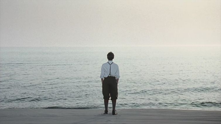 A man is standing on a beach looking at the ocean.