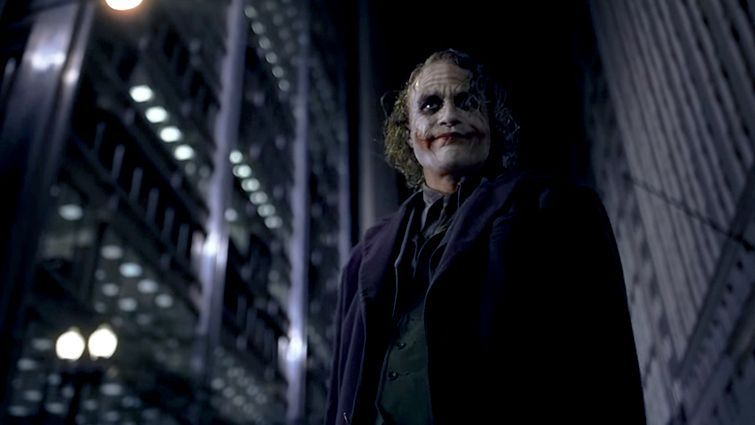 The joker is standing in the dark in front of a building.