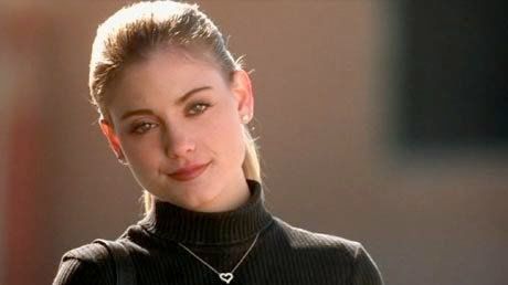 A woman wearing a black turtleneck and a necklace is looking at the camera.