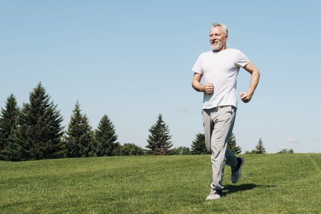 An older man is running in a park on a sunny day.