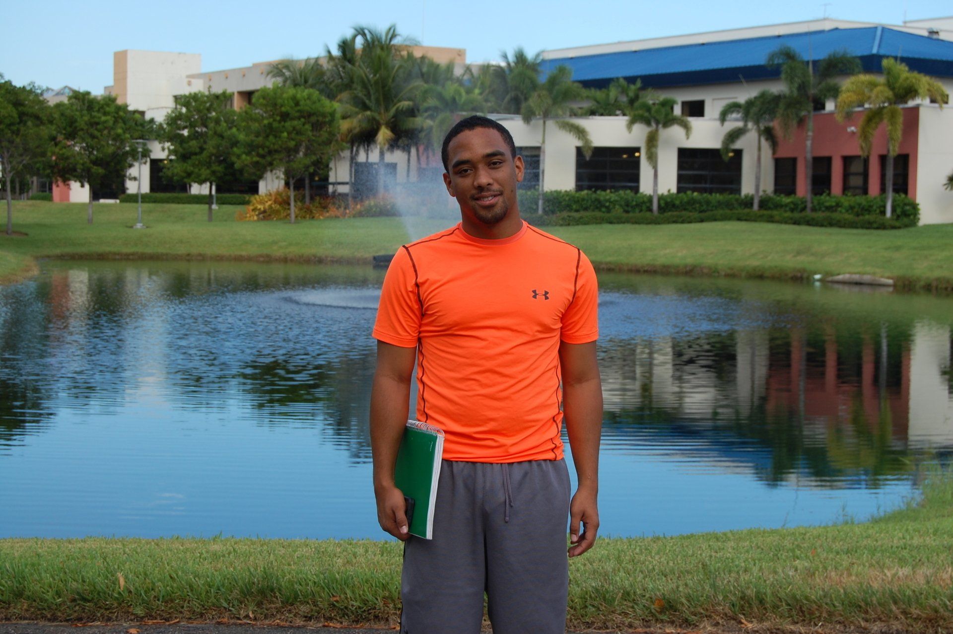 A man in an orange shirt is standing in front of a pond.