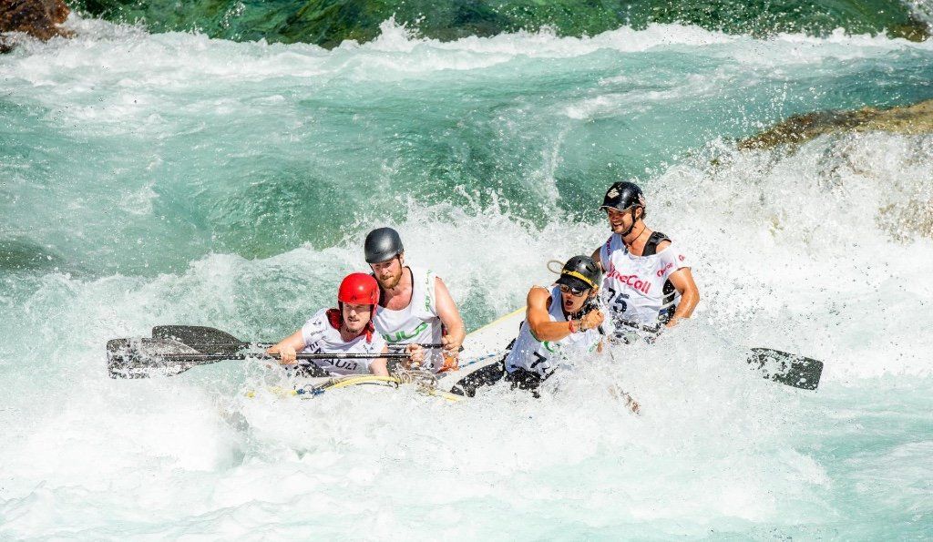 Four people in a raft navigate turbulent white water rapids.