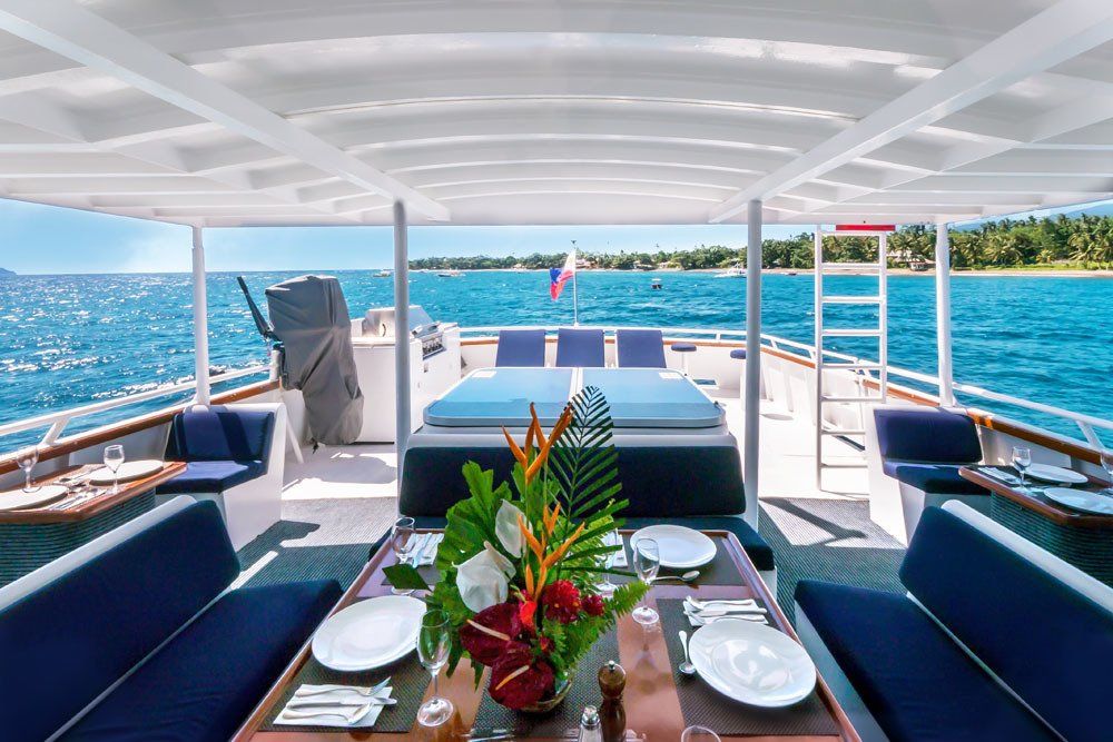 Luxury yacht deck with dining table, blue seating, and ocean view.