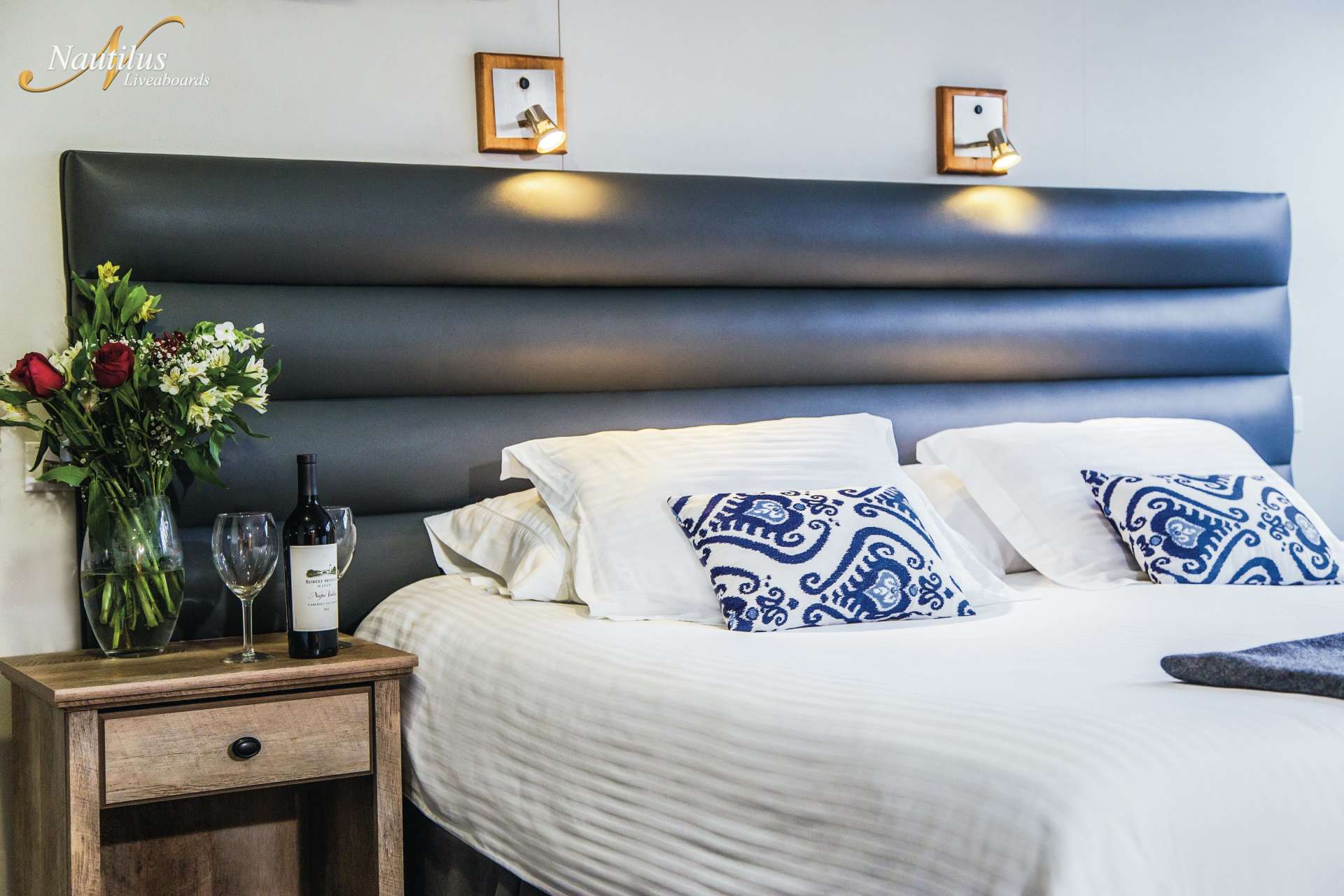 Bedroom with upholstered headboard, white bedding, nightstand, and flowers.