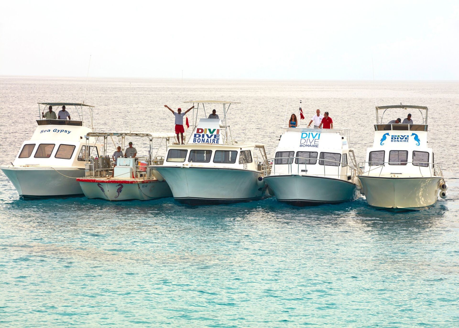 Five white boats floating in turquoise water, people on the boats.