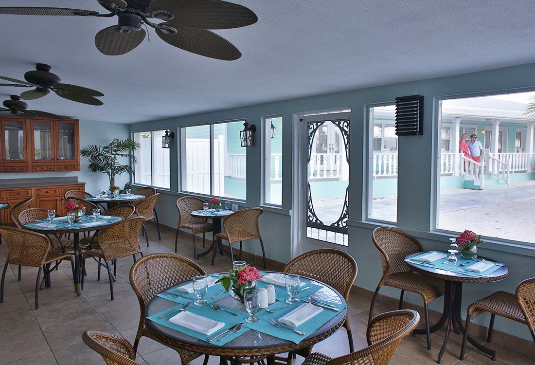 Restaurant interior with wicker chairs, small round tables, and large windows.