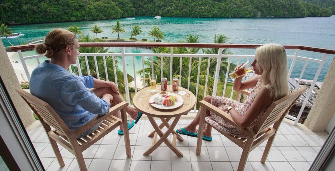 Couple on balcony with drinks, overlooking tropical lagoon.