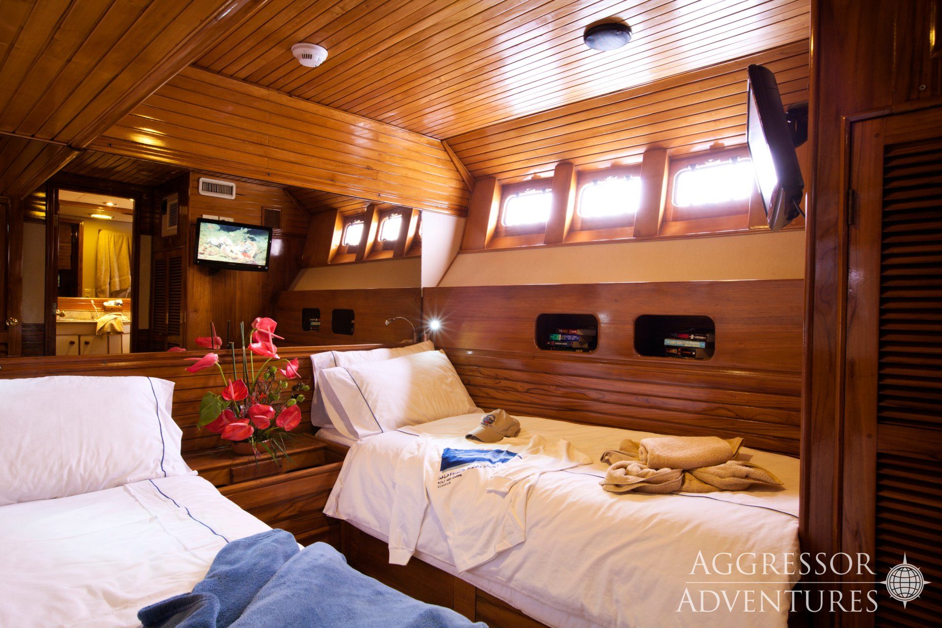 Bedroom on a boat with two twin beds, wood paneling, and a small TV.