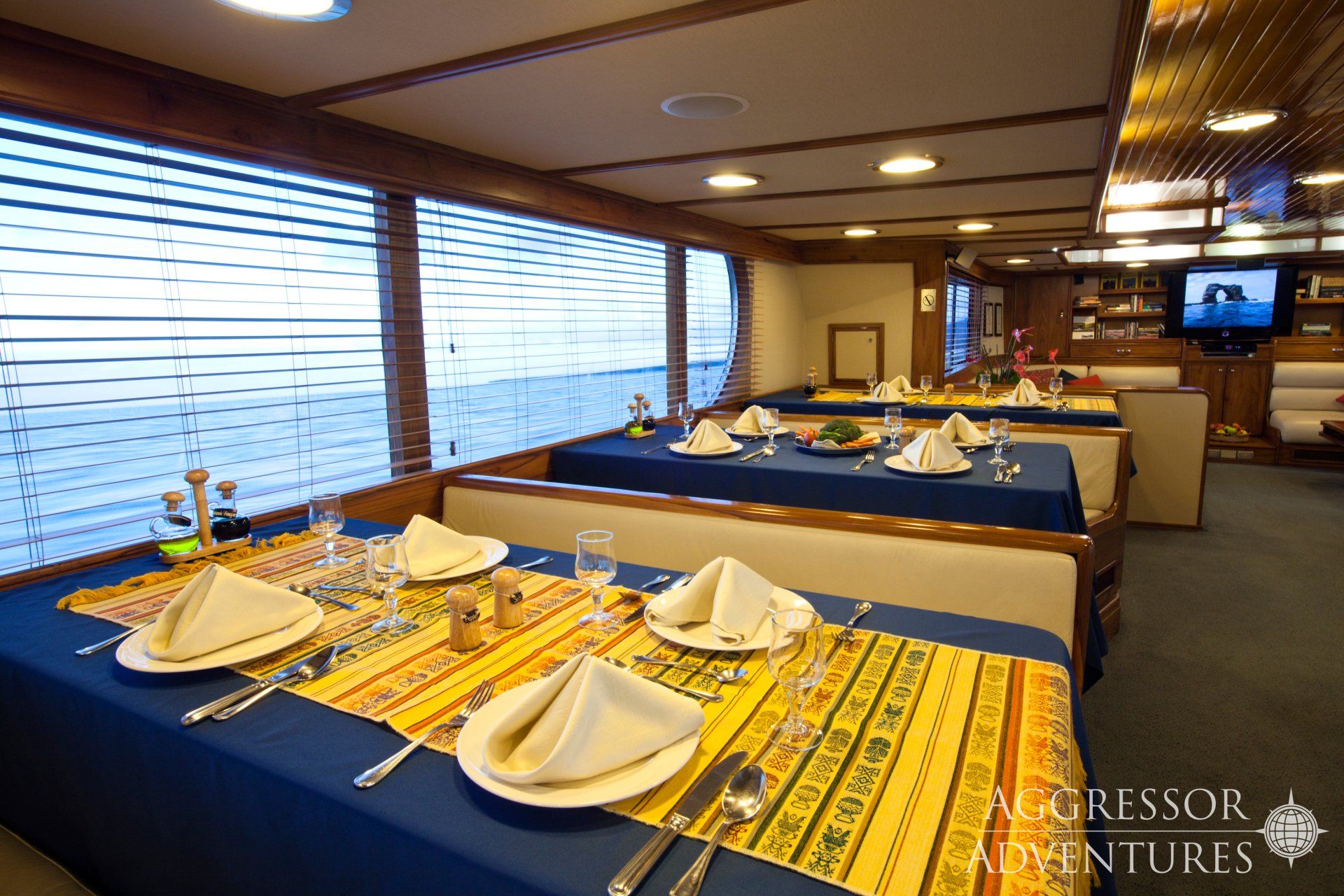 Dining area on a ship with tables set for meals, large windows, and a television.