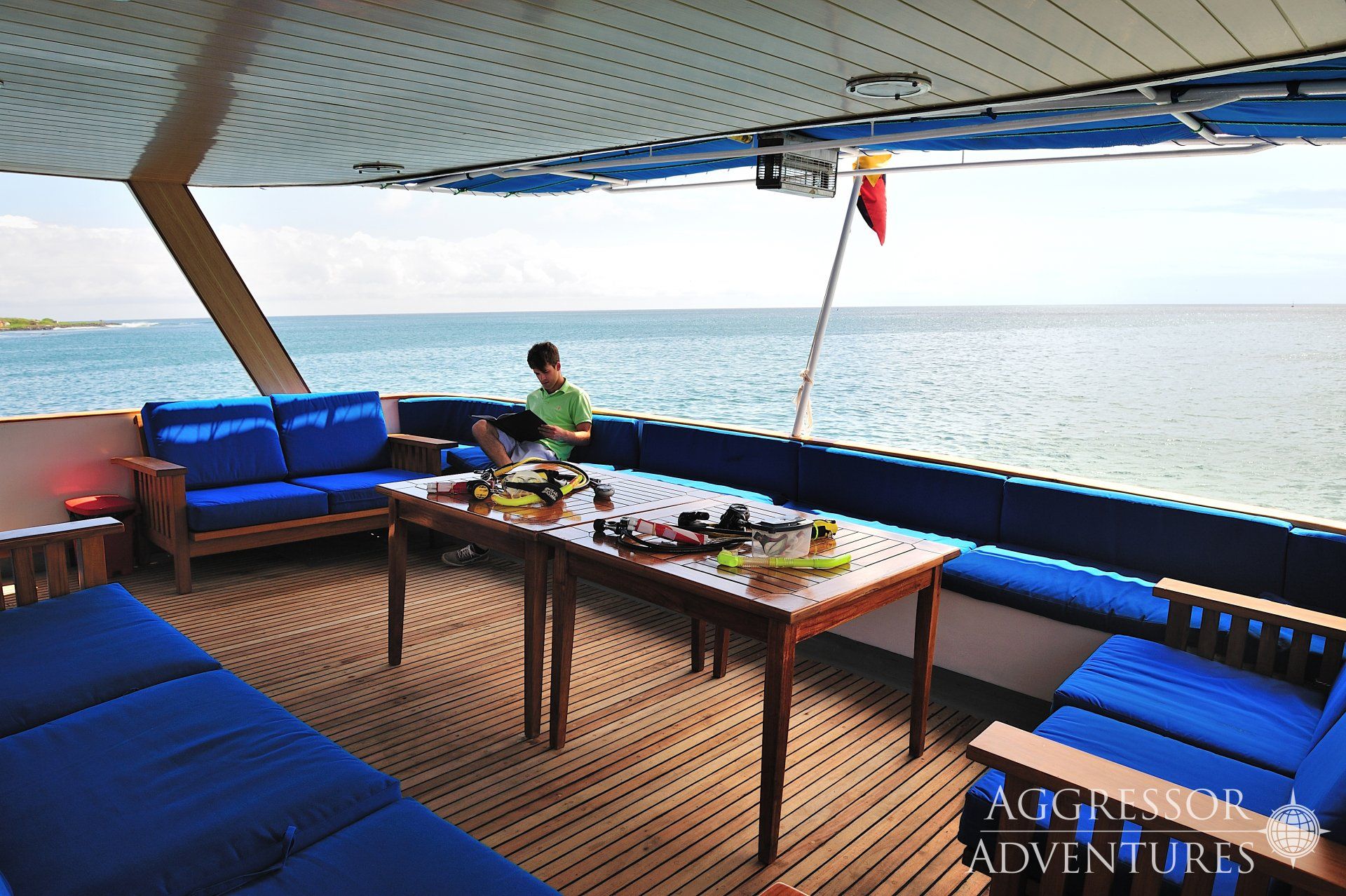 A person relaxes on a yacht's deck with blue cushions, a table, and ocean views.