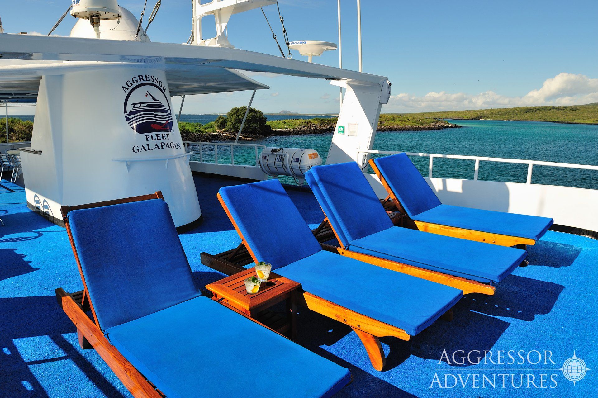 Lounge chairs on a blue deck of a boat with ocean view and blue sky.