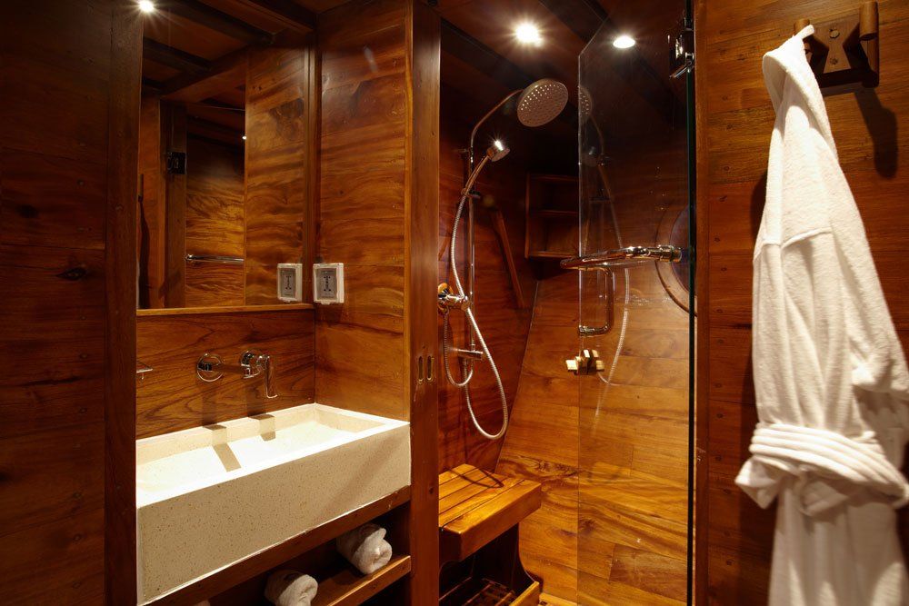 Bathroom with wood-paneled walls, a glass shower, a white sink, and a white bathrobe hanging on the wall.