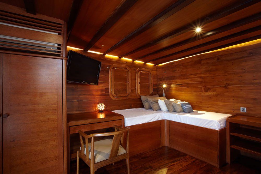 Wooden cabin interior with bed, desk, and TV. Walls and ceiling are paneled with wood.