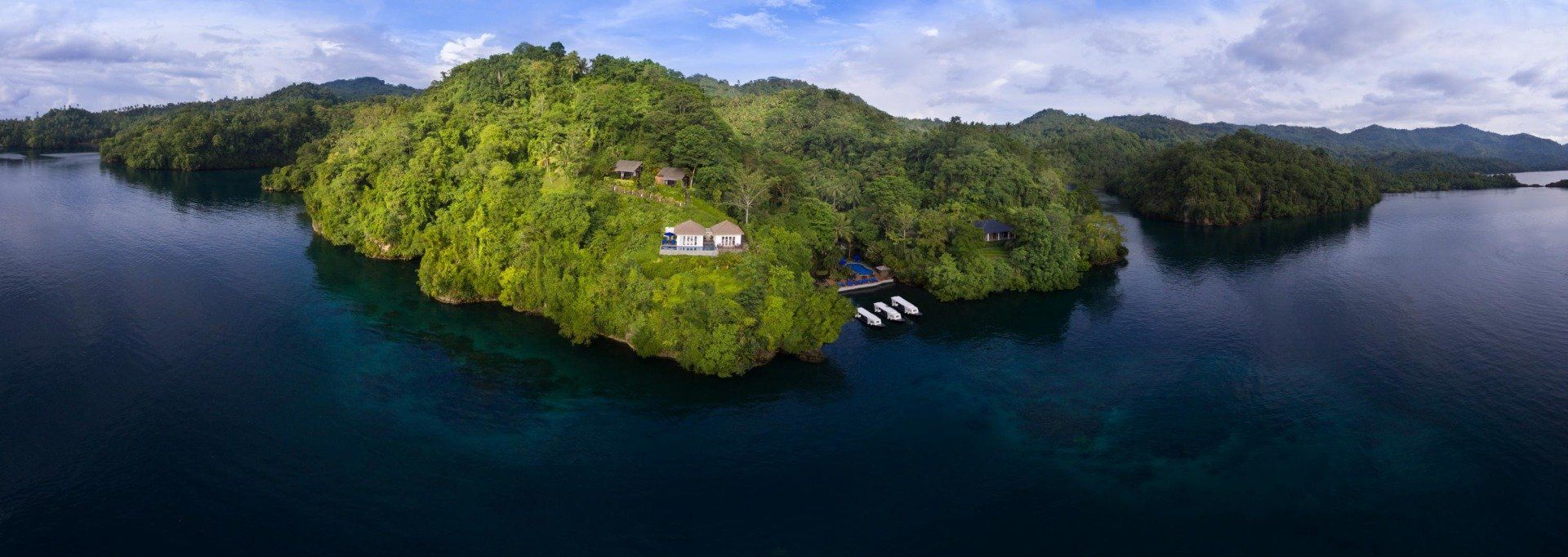 Aerial view of a lush green island surrounded by deep blue water, with white buildings and docks visible.