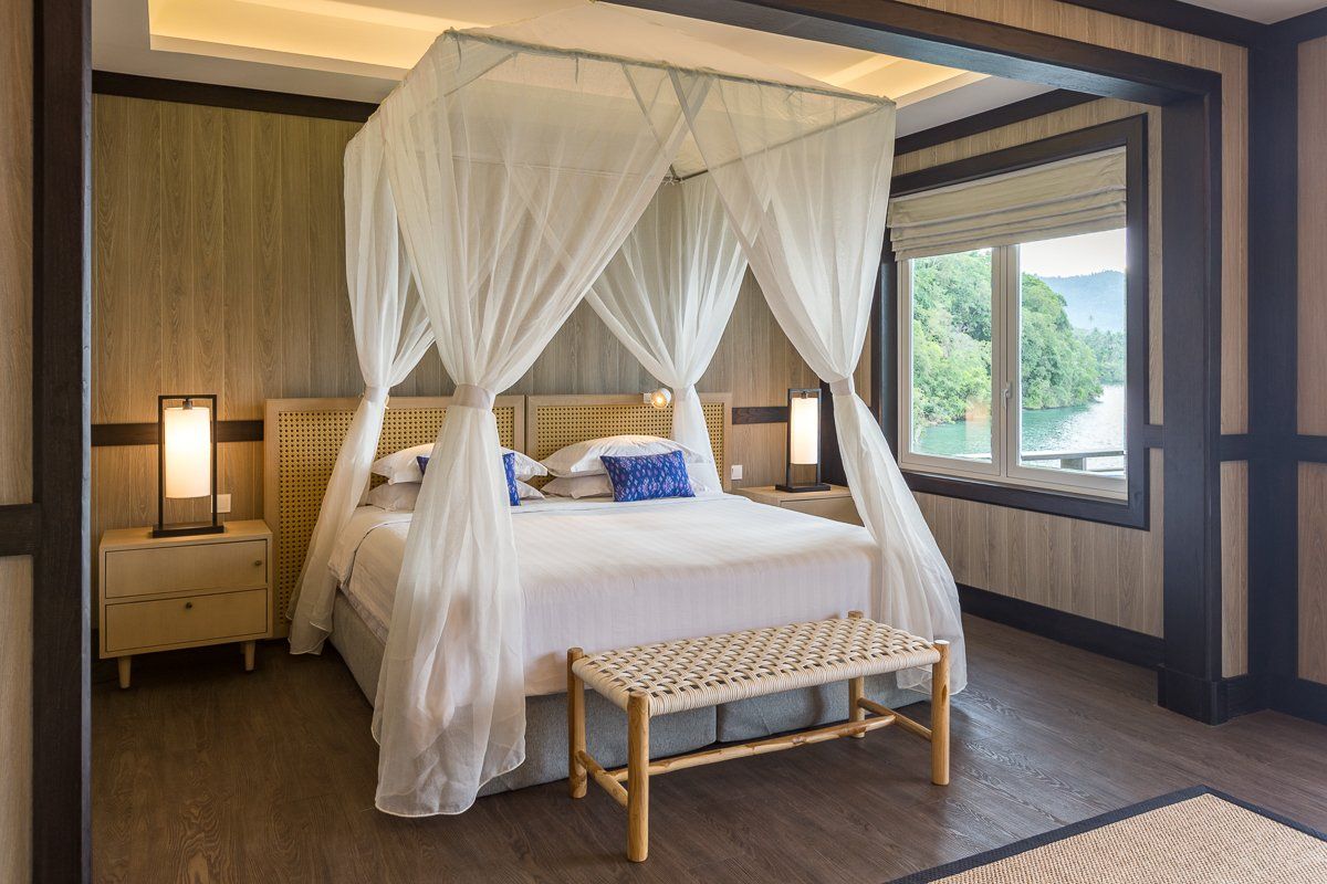 Bedroom with a canopy bed, bench, and large window overlooking a body of water.