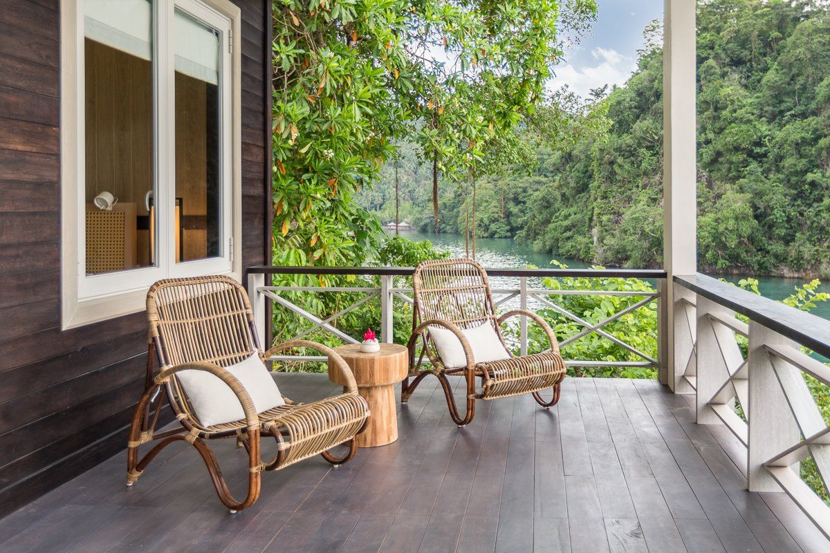 Two wicker chairs on a wooden porch overlooking a river and lush green trees.