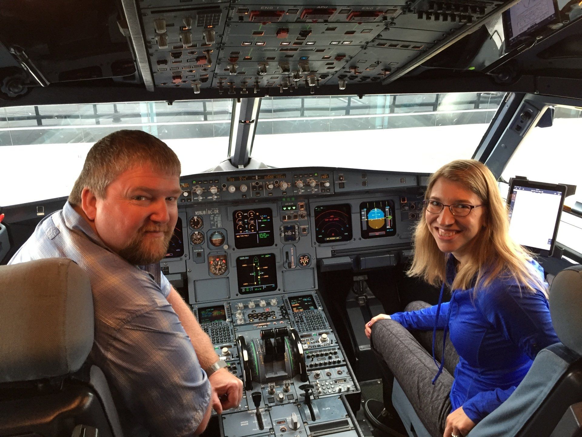 Two people smiling in an airplane cockpit. The man is on the left, woman on the right, cockpit instruments in the background.