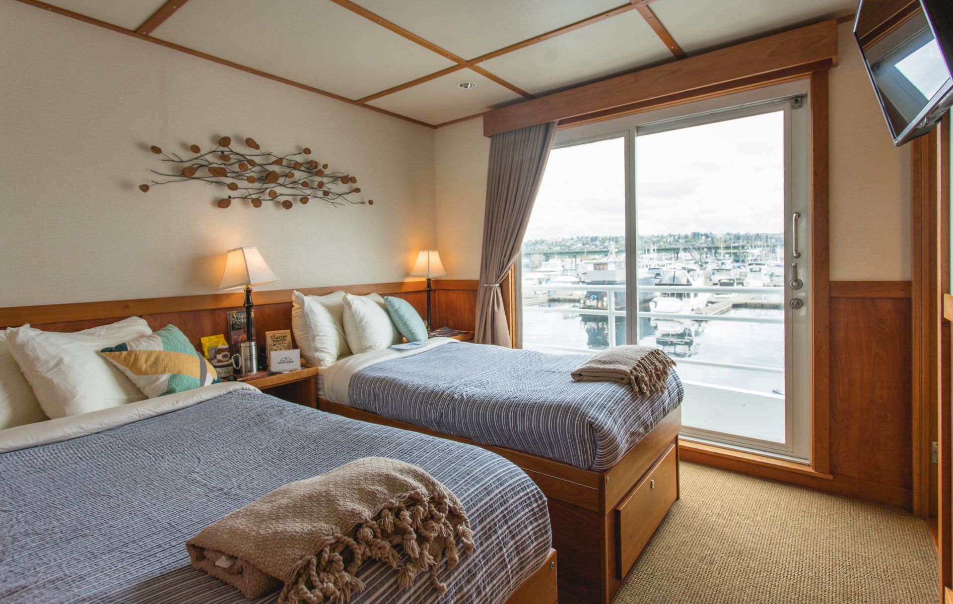 Bedroom with two beds, large window overlooking a cityscape. Blue and white bedding, wooden accents.