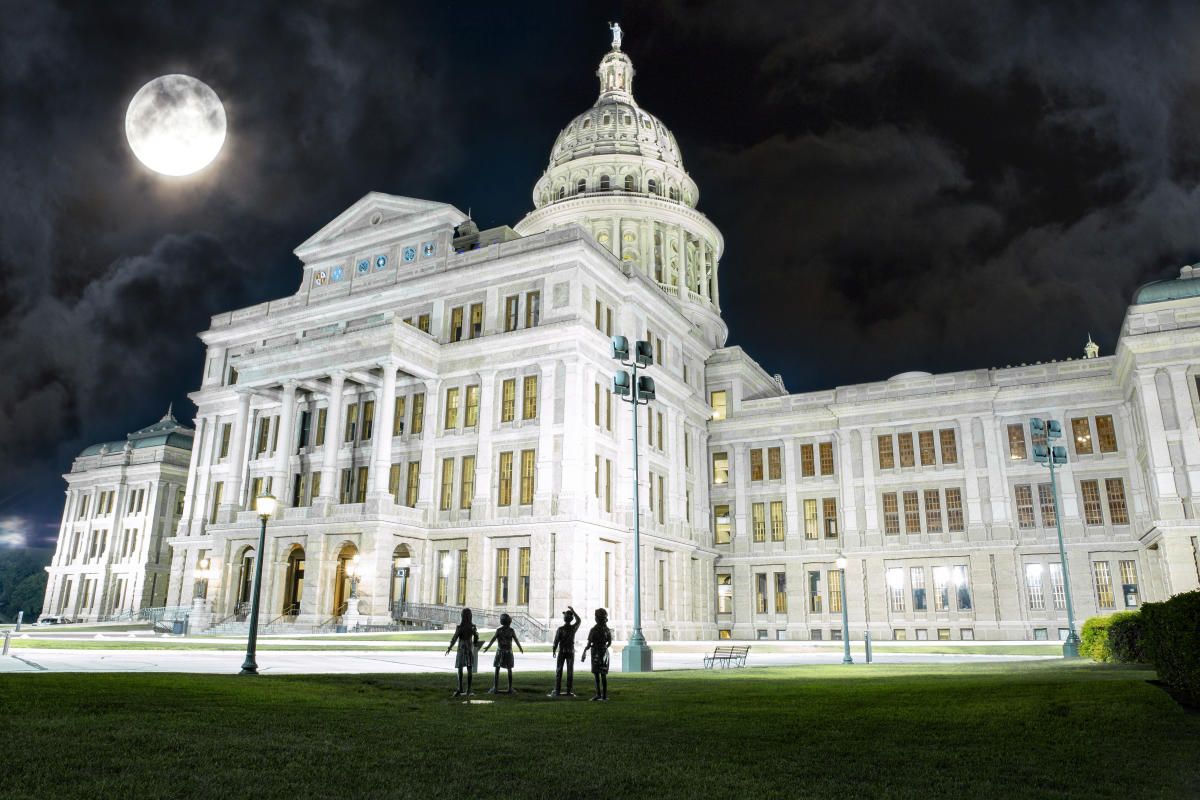Texas State Capitol building at night with full moon; three silhouetted figures on the lawn.