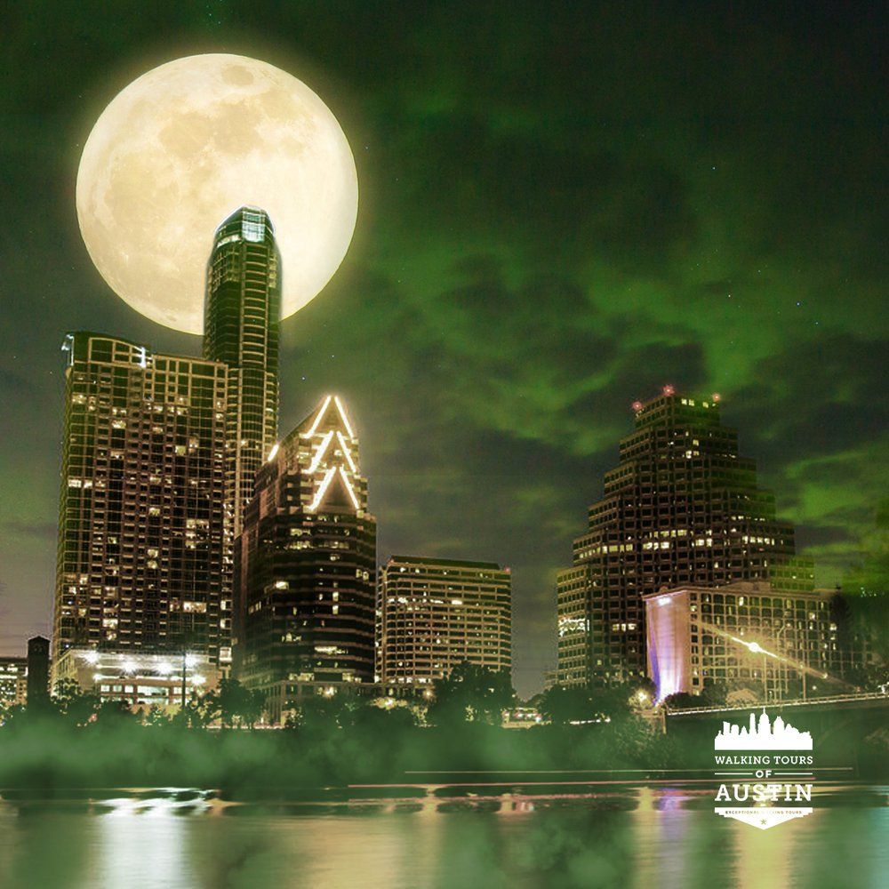 Austin skyline at night, illuminated by a full moon and green sky reflected in the water.