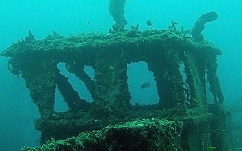 Underwater view of a ship's structure, covered in marine growth, with open windows, in blue water.