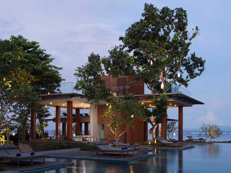 Resort pool area at dusk with lounge chairs, trees, and a wooden structure.