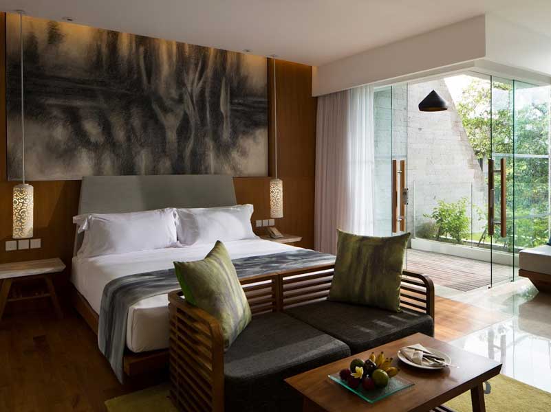 Hotel bedroom with a bed, small sofa, and a sliding glass door to a balcony.