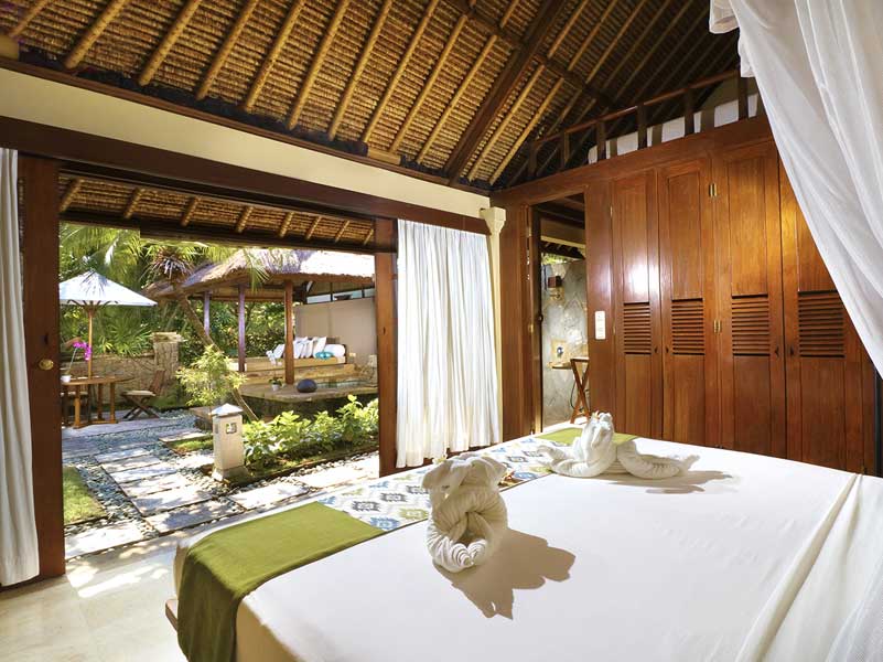 Bedroom with open doors to a patio, a bed with folded towels, and wooden furniture.