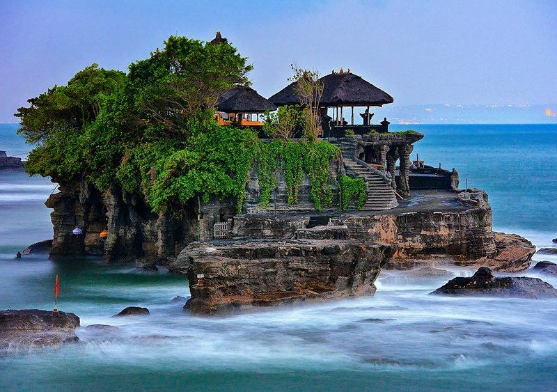 Temple on a rocky island in the ocean with clear water and cloudy sky.