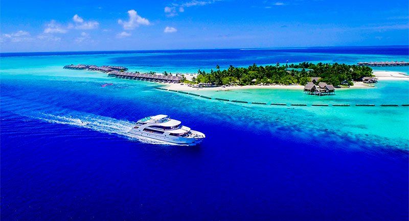 Luxurious boat cruising near a tropical island with turquoise water and overwater bungalows.