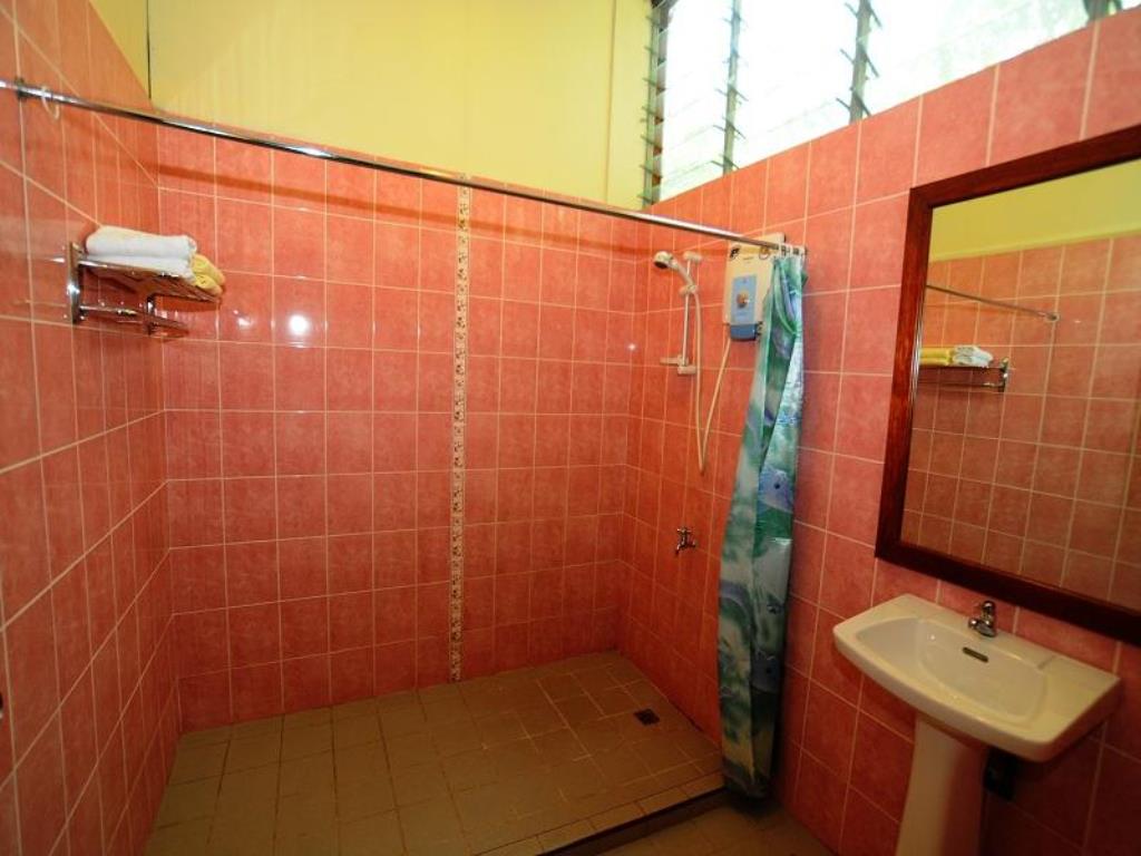 Pink tiled shower stall with shower curtain, sink, and mirror. Towel rack with folded towels on the wall.