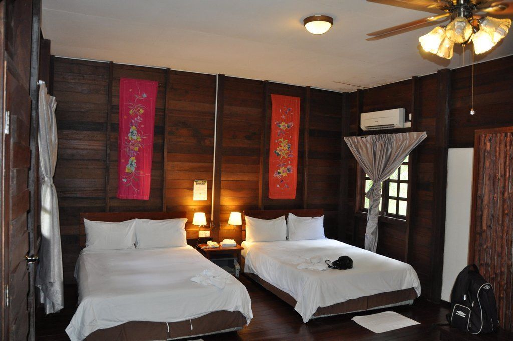 Bedroom with two double beds, wooden walls, decorative banners, and ceiling fan.