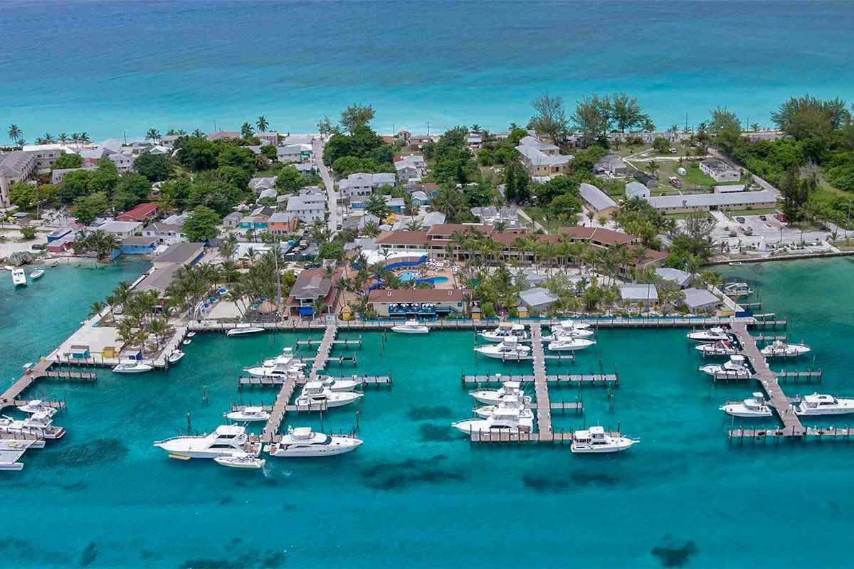 Marina with boats docked, buildings, and turquoise water.
