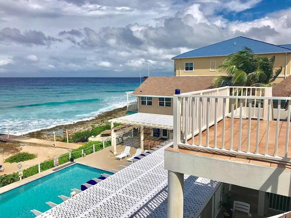 Poolside view overlooking ocean, buildings with light-colored walls and blue roof.
