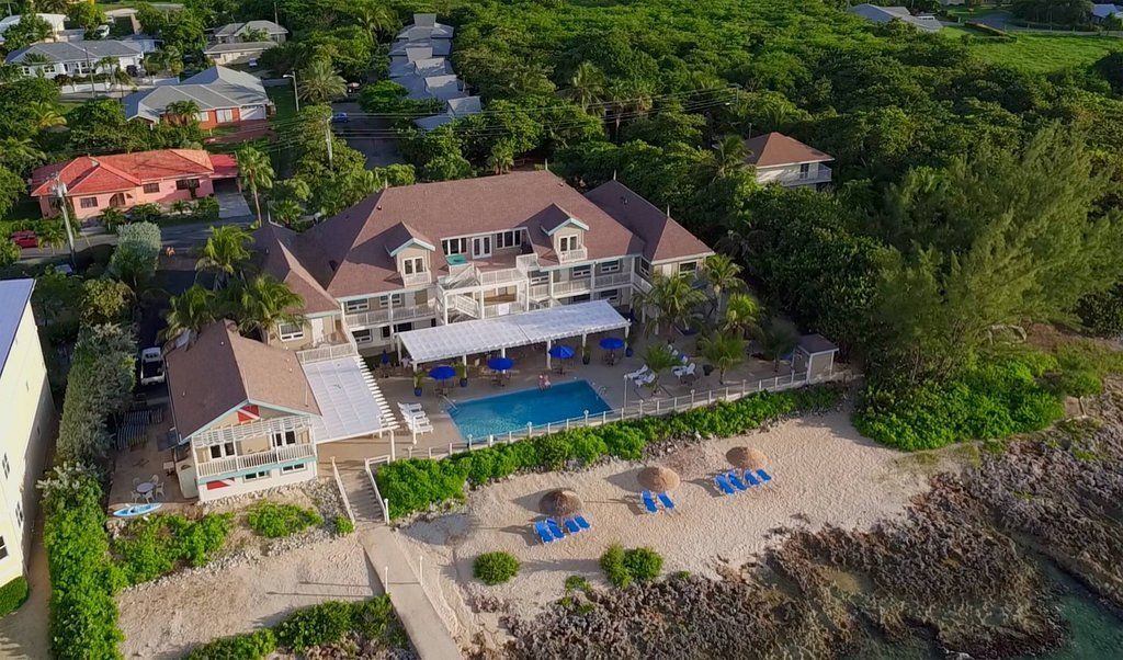 Beachfront resort with pool, beach chairs, and large building surrounded by trees.