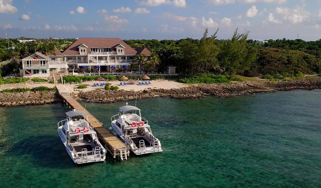 Boats docked at a pier in front of a multi-story building on the coast with clear turquoise water.