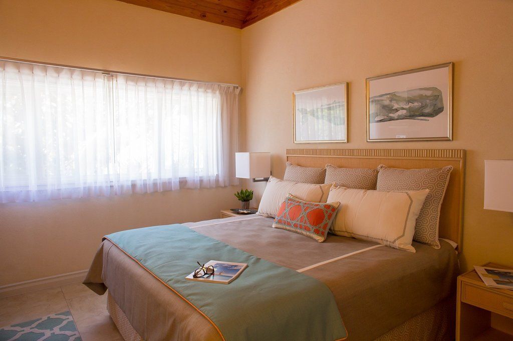 Bedroom with bed, teal throw, pillows, artwork, sheer curtains, bedside tables, and lamps.