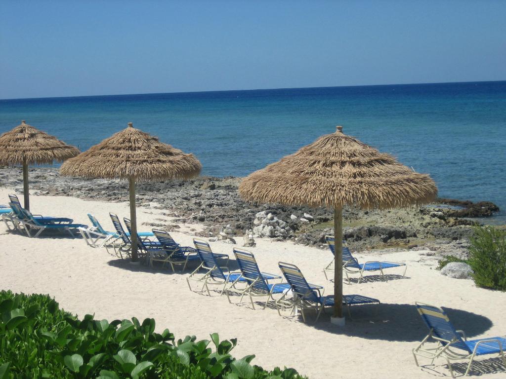 Beach scene with thatched umbrellas, blue lounge chairs, white sand, and turquoise water.