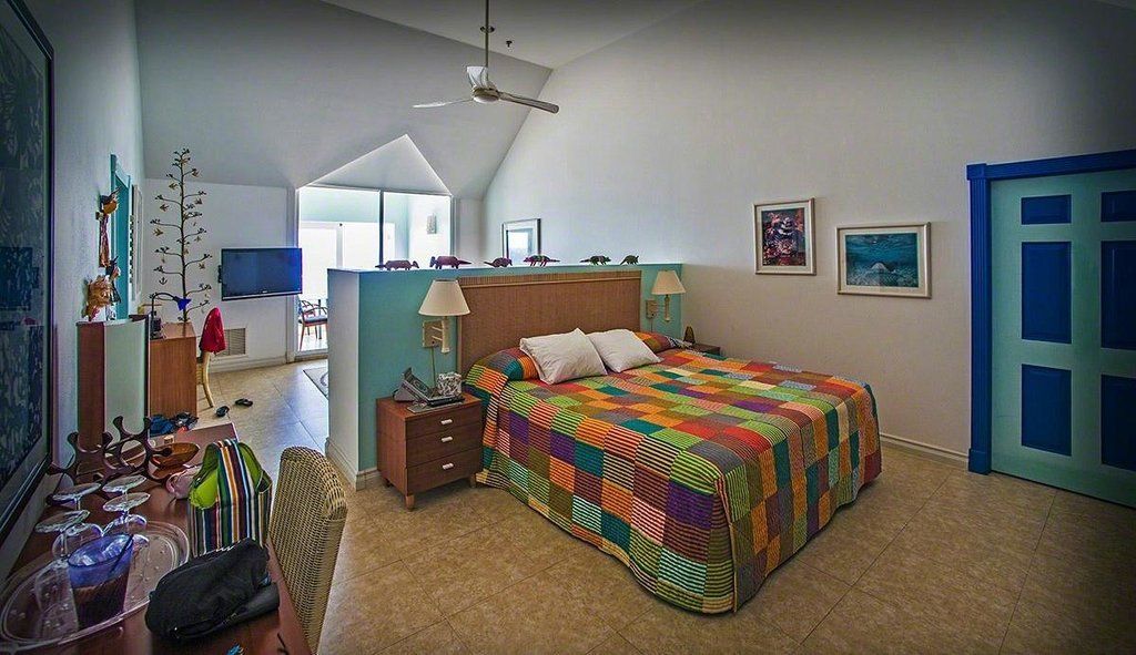 Bedroom with colorful quilt, wooden furniture, blue door and wall accents, and art.