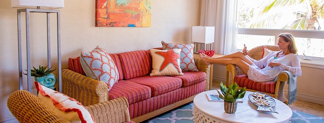 Living room with red sofa, wicker furniture, woman relaxing in chair by the window.