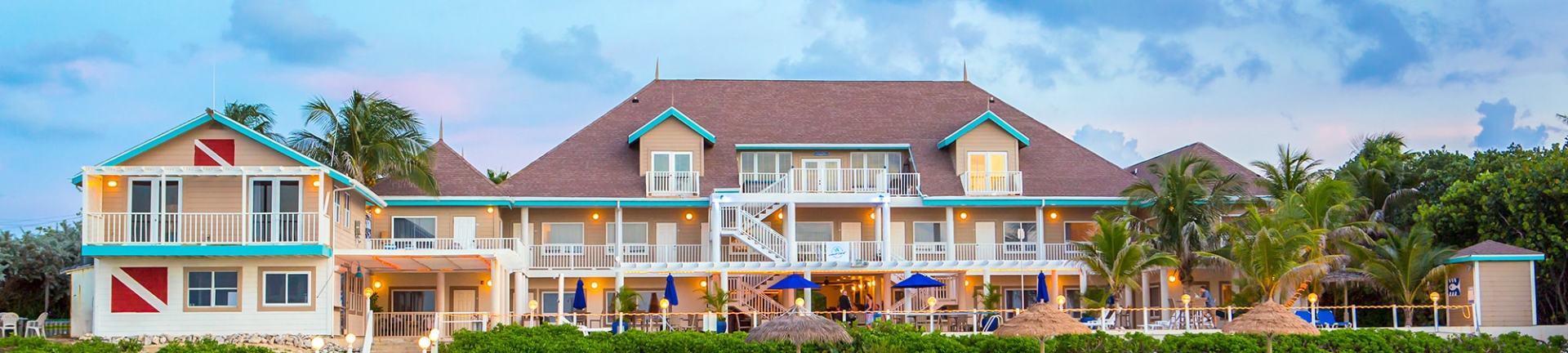 Tropical resort with beige buildings, red roof, balconies, and green trim. A dive flag is visible.