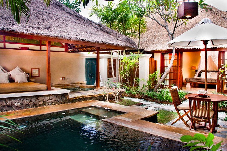 Pool and patio area of a Balinese villa with thatched roof, pool, and seating areas.